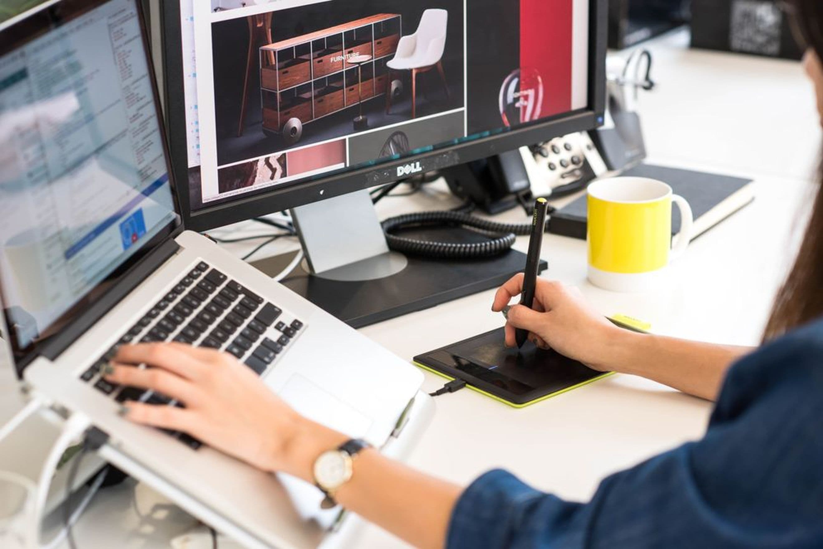 A web designer at our ecommerce development agency refining product visuals on a digital drawing tablet and laptop.